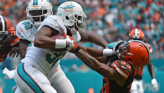 Dolphins running back Kenyan Drake (32) stiff-arms his way past Browns defender Jordan Poyer on a first-half carry.