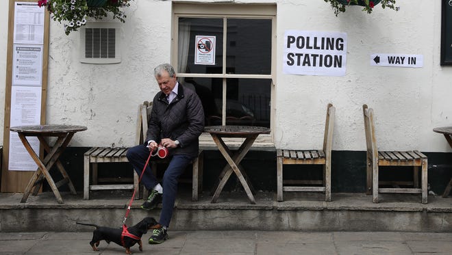 A man sits with his dog Dylan outside a Polling Station at the Anglesea Arms pub  in London.