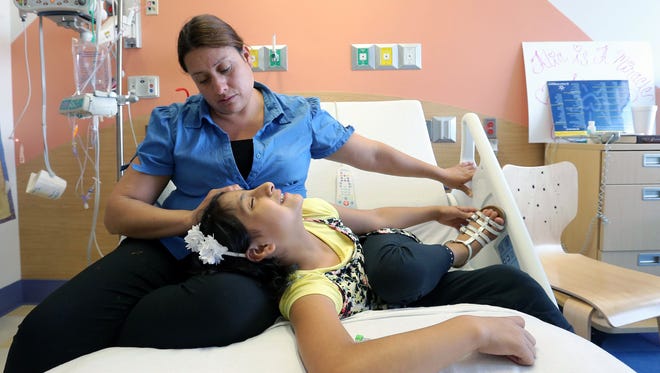 Maria Elena de Loera strokes her daughter Alia Escobedo’s hair at El Paso Children’s Hospital. De Loera, a Mexican citizen, is fighting to stay in the United States to be by her daughter’s side as she undergoes treatment for small cell osteosarcoma.