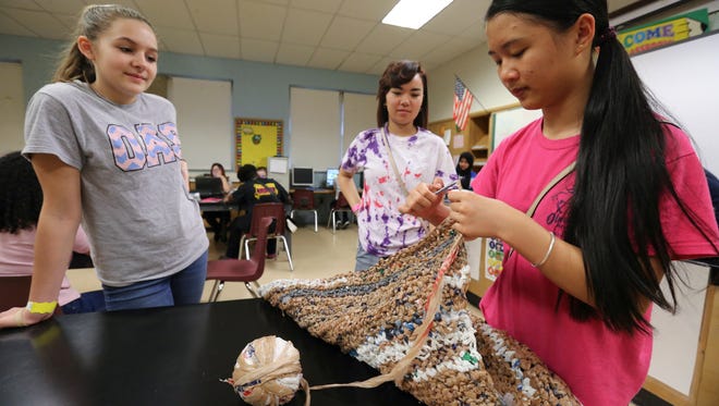 Deyi Chen, right,  knits a mat out of plastic grocery bags at Olmsted Academy South as classmates Chloe Winchell, left, and Tammeka Mai, right, look on.  The mats knitted by the students will ultimately be given to those who are homeless to use.