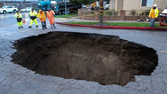 Inspectors examine a sinkhole, on Feb. 18, 2017, in Studio City, north of Los Angeles. Two vehicles fell into the 20-foot sinkhole on Friday night and firefighters had to rescue one woman who escaped her car but was found standing on her overturned vehicle.