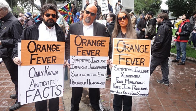 Rob Adler (left) Mike Stutz (middle) and Laurel Trotter, painted their faces orange and held 'Orange Fever,' signs for the 'Not my President's Day' rally in front of City Hall steps in Los Angeles, Calif. on Feb. 21, 2017. 'Fear is 'contagious,' said Stutz. 'Don't catch the orange fever. Embrace your fellow man.'