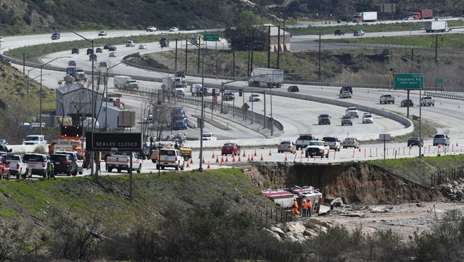 Traffic passes along the scene Feb., 18, 2017, where a tractor trailer and a San Bernardino County Fire Department fire engine fell on Friday from southbound Interstate 15 where part of the freeway collapsed due to heavy rain in the Cajon Pass, Calif.,