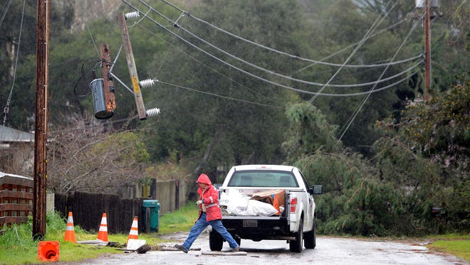A worker starts repair work where trees battered by heavy winds pulled power lines which broke a pole in rural Salinas, Calif., Feb. 17, 2017.