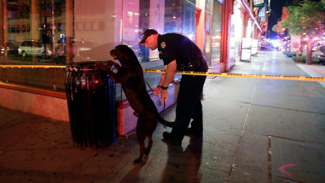 A New York City Police emergency services officer and his dog check a garbage can near the scene of an explosion in Chelsea.